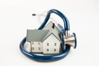Blue stethoscope wrapped aroud tiny house model on white background.jpeg