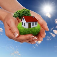 Human hand against blue sky background and house